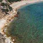 Aerial shot of a serene beach cove with clear turquoise waters and rocky shoreline.